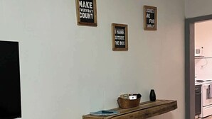 A room with a wooden shelf holding a bowl and a book, a flat-screen TV mounted on the wall, and three motivational signs. - Historic Mt. Iron Apartment (Mountain Iron)