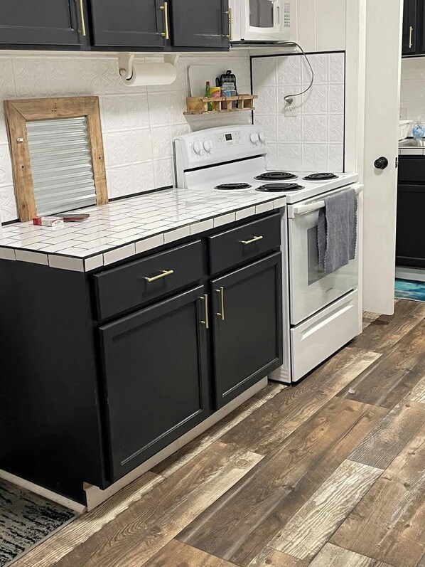 A kitchen with a white stove, black cabinets, and a wooden floor. - Historic Mt. Iron Apartment (Mountain Iron)