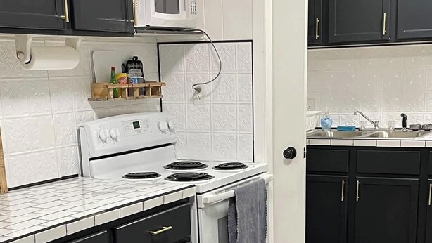 A kitchen with black cabinets, a white stove, and a wooden floor. - Historic Mt. Iron Apartment (Mountain Iron)