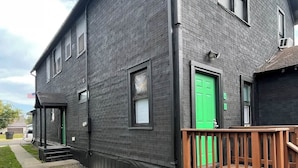 A two-story building with a green door, a wooden deck, and a sidewalk leading to the entrance. - Historic Mt. Iron Apartment (Mountain Iron)