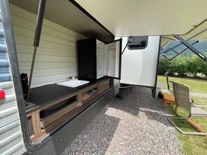 A compact RV interior with a kitchenette, a sink, and a window providing a view of the outdoors.
