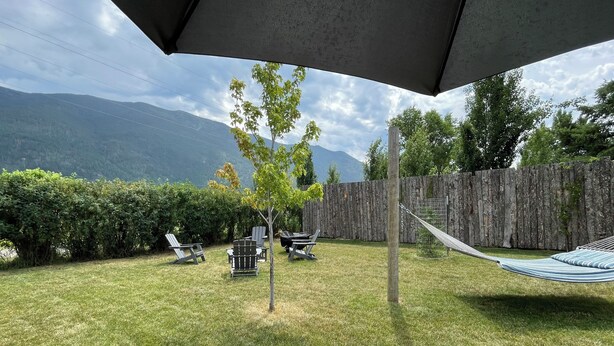 A backyard with a wooden table, a hammock, and two lawn chairs.