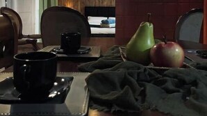 Un comedor con una mesa preparada para dos personas, que incluye una bandeja con una taza, una pera y una manzana.