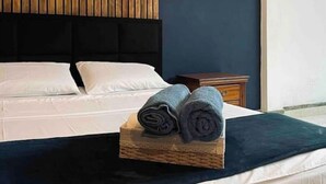 Una cama bien hecha con sábanas blancas, un cabecero oscuro y una mesita de madera con un pequeño reloj.