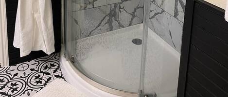 A bathroom with a glass-enclosed shower, marble tiles, a white robe hanging on a rack, and a black bathtub.