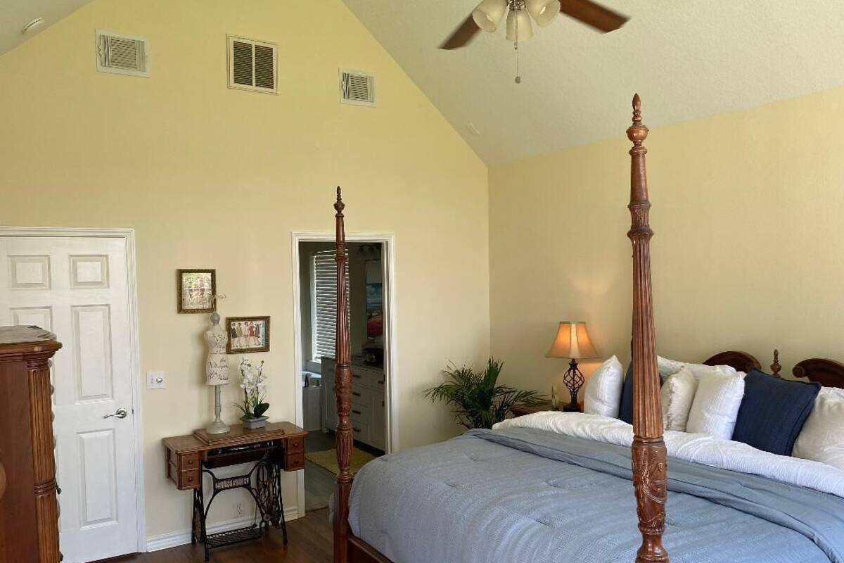 A bedroom with a four-poster bed, a desk with a lamp, and a ceiling fan.