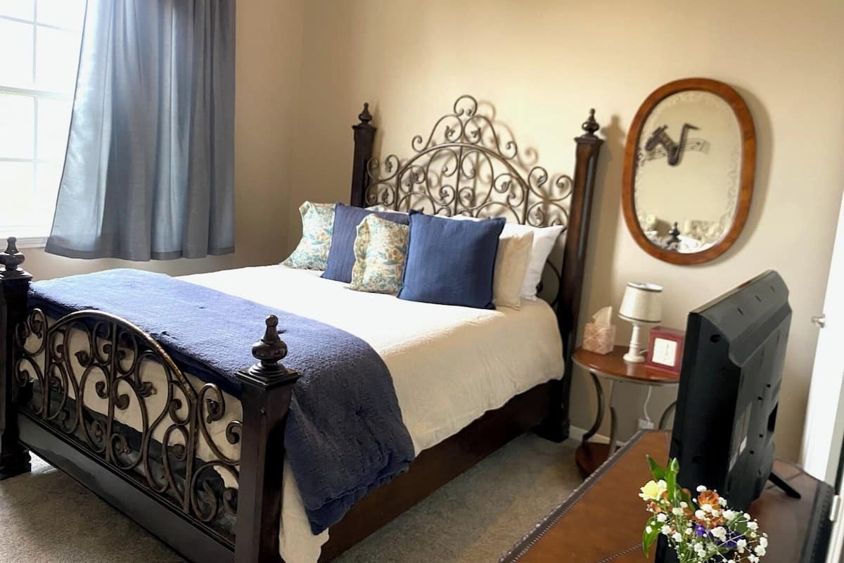 A bedroom with a bed, a bedside table with a lamp, a mirror, and a TV.