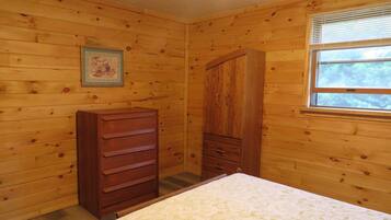 A wooden-paneled room with a bed, a dresser, and a window with blinds.