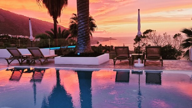 Area piscina con lettini e vista sull'oceano al tramonto.