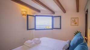 Camera da letto con un letto, una finestra vista mare, una lampada a parete e un quadro incorniciato.