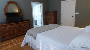 A bedroom with a large bed, a dresser, a television on the dresser, and a door leading to another room.