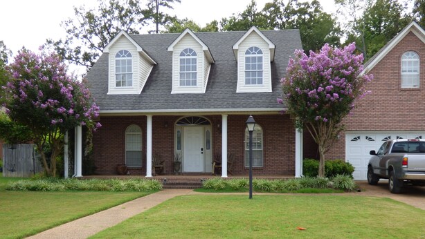 A two-story brick house with a front porch, a garage, and a driveway.