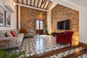 Una sala de estar con una pared de piedra, un sofá, un sillón rojo, un televisor y un suelo estampado.