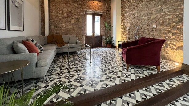 A living room with a stone wall, a patterned floor, a sofa, a red armchair, and a coffee table. - Beautiful and spacious 3 bedrooms in the Old Town with balcony (Ciudad de Panamá)