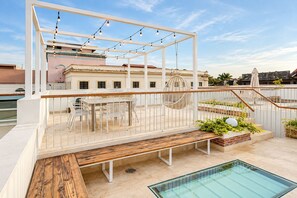 A rooftop terrace with a pool, outdoor seating, and string lights.