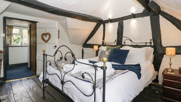 A bedroom with a four-poster bed, a wooden floor, and a sloped ceiling with exposed beams. - Avonmede (Tewkesbury)