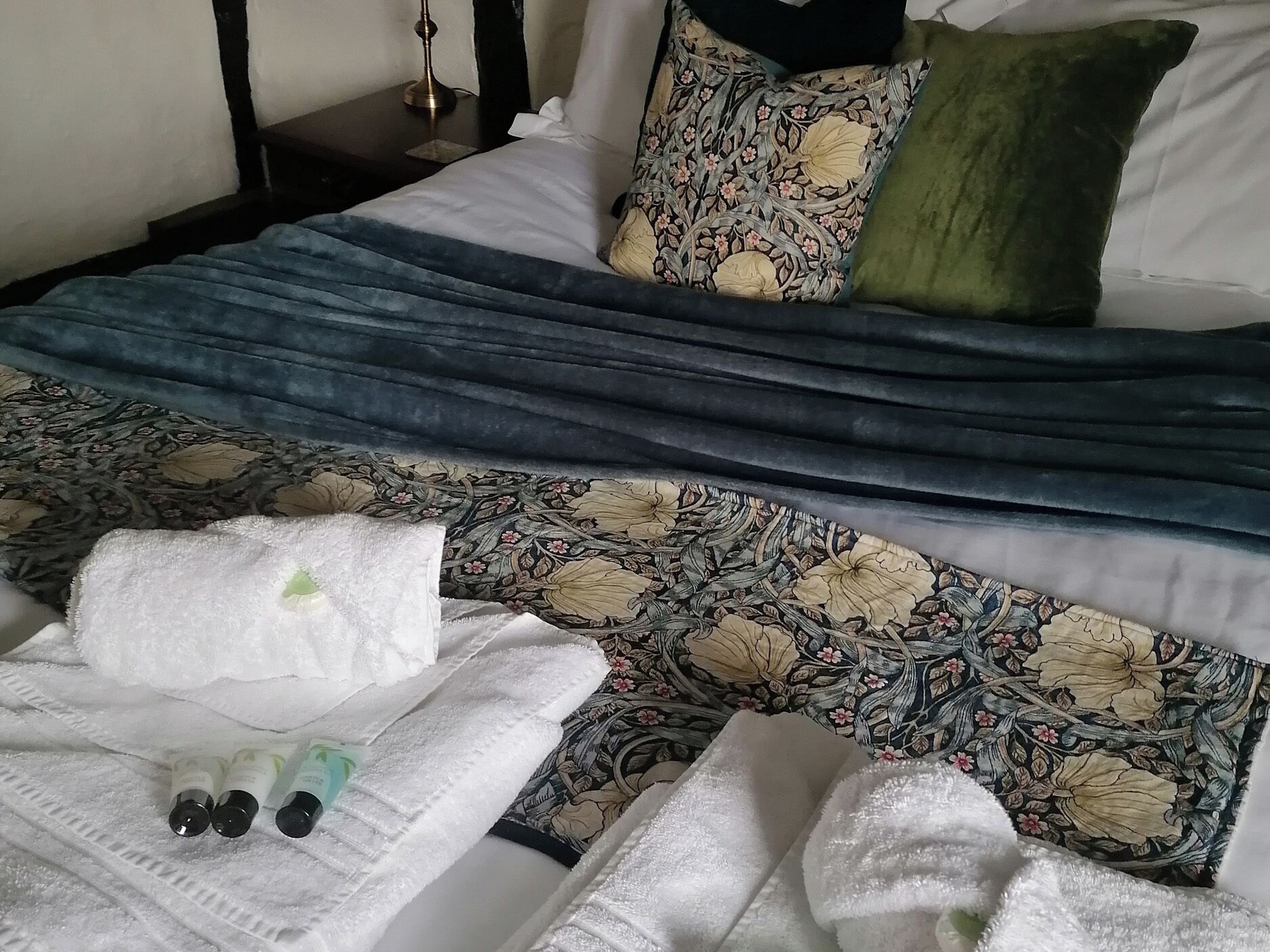 Uma cama com colcha estampada de flores, manta azul e travesseiro verde.