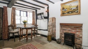 A traditional room with exposed beams, a fireplace, a dining table with chairs, and a painting on the wall. - Avonmede (Tewkesbury)