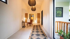 Un couloir avec un tapis à motifs, une chaise, une petite table et un luminaire suspendu.