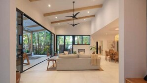 Un vaste espace de vie comprenant un grand canapé, un ventilateur de plafond et une vue sur l’extérieur grâce à de grandes fenêtres.