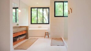 Une salle de bain moderne dotée d’une grande fenêtre, d’un banc en bois et d’une étagère intégrée où sont rangées les serviettes.