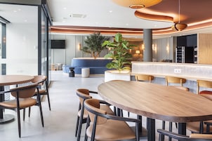 Un moderno vestíbulo de hotel con una mesa redonda de madera y sillas, un sofá azul y una planta grande en maceta.