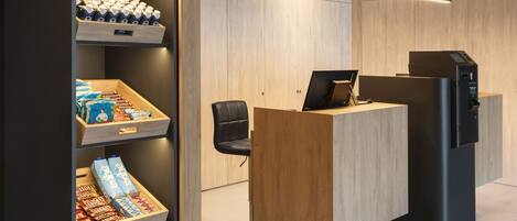 A reception area with a wooden desk, a black chair, and a shelf with bottled water and snacks.