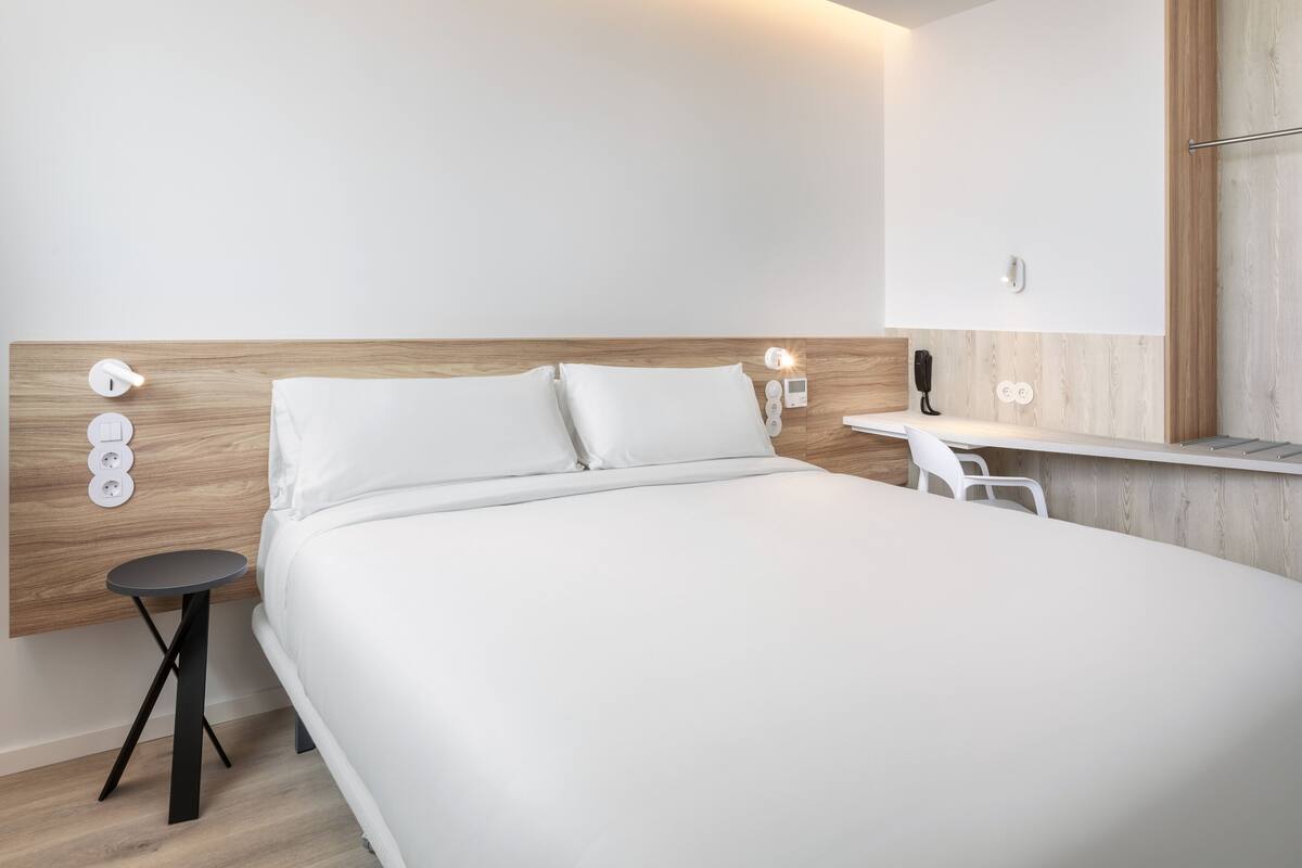 Une chambre d’hôtel moderne avec un grand lit, des tables de chevet, un petit bureau et un miroir.