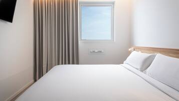 Habitación de hotel con cama, ventana, cortinas, televisor montado en la pared y termostato.