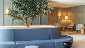 A modern lounge area with a blue sofa, a small table, a lamp, and a decorative tree. - B&B Hotel Vila do Conde  (Vila do Conde)