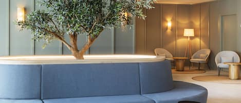 A modern lounge area with a blue sofa, a small table, a lamp, and a decorative tree.