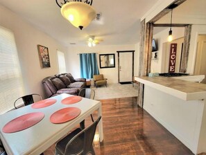 A dining area with a table set for four, a brown leather sofa, and a kitchen area with a hanging light fixture. - Relaxing KING bed & 2 queen beds 1 mile to Downtown Riverwalk (San Antonio)