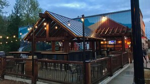 A wooden outdoor seating area with tables and chairs, a railing, and string lights. - Downtown Snoqualmie Home - Hot Tub, Fully Fenced Yard - Pet Friendly! (Snoqualmie)