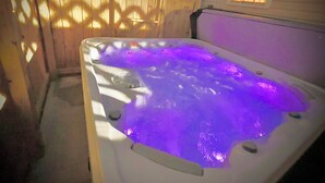 Un jacuzzi con iluminación púrpura, rodeado por una valla de madera y una casa al fondo.