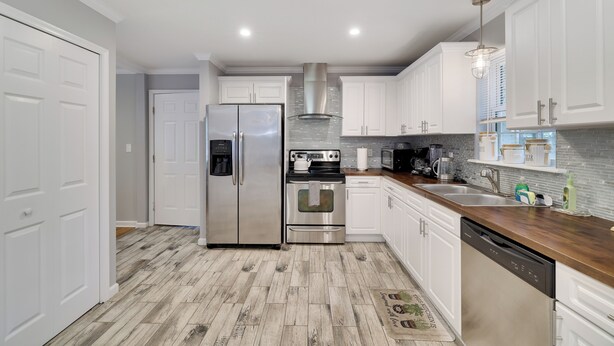 Una cocina moderna con armarios blancos, electrodomésticos de acero inoxidable y piso de madera.