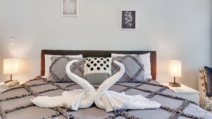 Una cama bien hecha con un edredón fruncido, dos lámparas de noche y un cuadro enmarcado sobre la cama.