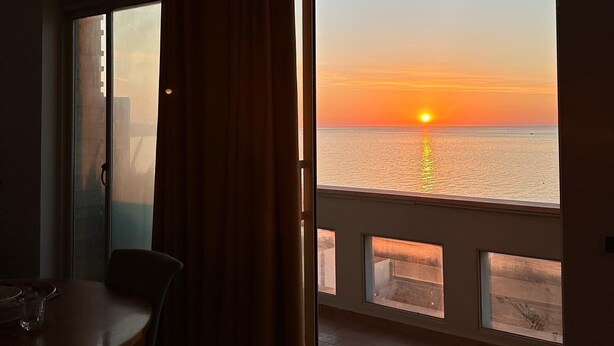 A room with a large sliding glass door leading to a balcony with a view of the sunset over the water. - Modern and bright apartment located on the Catania waterfront. (Catania)