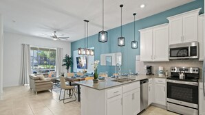 A modern kitchen with white cabinets, stainless steel appliances, and pendant lighting.
