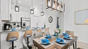 A modern kitchen with white cabinets, a stainless steel refrigerator, and a dining area with a wooden table set for four.