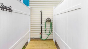 Un espacio exterior pequeño y cerrado con un suelo de madera, una manguera y una puerta azul.