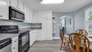 Una cocina moderna con armarios blancos, una estufa negra y una zona de comedor con sillas de madera y una mesa.
