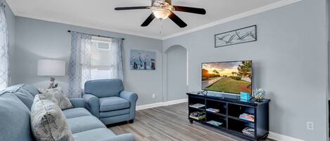 A living room with a ceiling fan, a sofa, a chair, a TV, and a bookshelf.