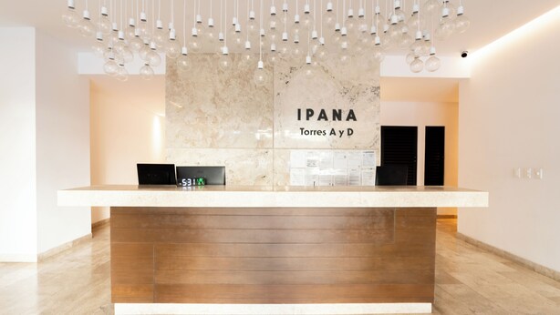 A reception desk with a marble wall, a digital clock, and hanging light fixtures. - Ipana by Casago (Playa del Carmen)