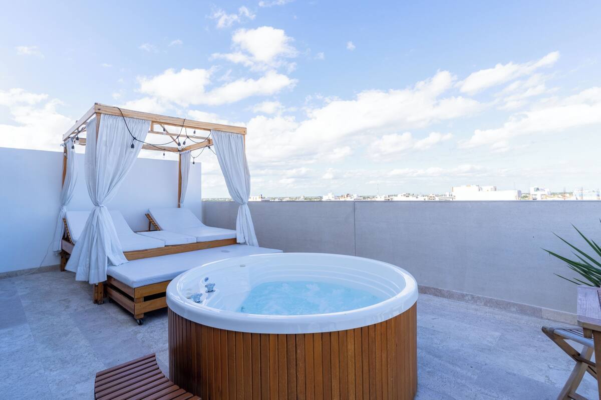 Terraço no telhado com cama de madeira coberta, uma banheira de hidromassagem e vista para o horizonte da cidade.