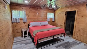 Une chambre à coucher aux murs lambrés, avec un lit, deux fenêtres avec des rideaux, une table de chevet et une porte.