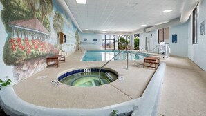 An indoor swimming pool with a mural, two lounge chairs, and a hot tub.