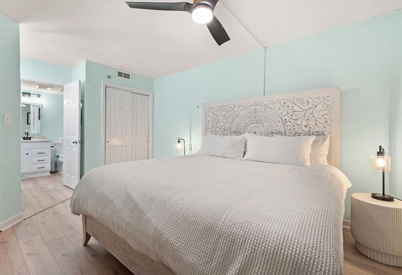 Ein Schlafzimmer mit einem großen Bett, einem Deckenventilator und einem Nachttisch mit einer Lampe.