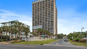 A tall, modern hotel with a grid of balconies, a well-maintained lawn, and palm trees.