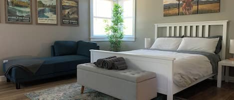 A bedroom with a bed, a bench, a sofa, a window, and wall art.