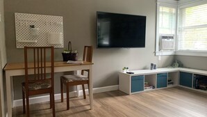 A room with a wooden dining table, two chairs, a television mounted on the wall, a window with blinds, and a small shelf with items. - The Hyde Park Hideaway | Centrally-Located | Cozy (Austin)